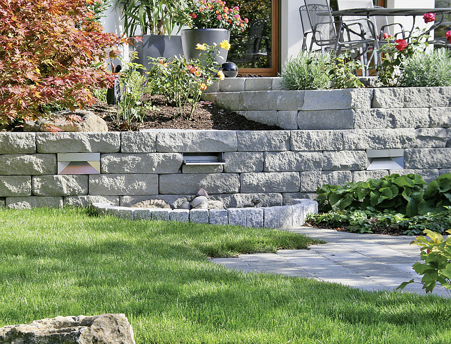 Gartenmauer SANTURO Weinbergmauer in der Farbe Naturgrau mit SANTURO Wasserfall und FOCUS Leuchten-Mauermodul im Garten