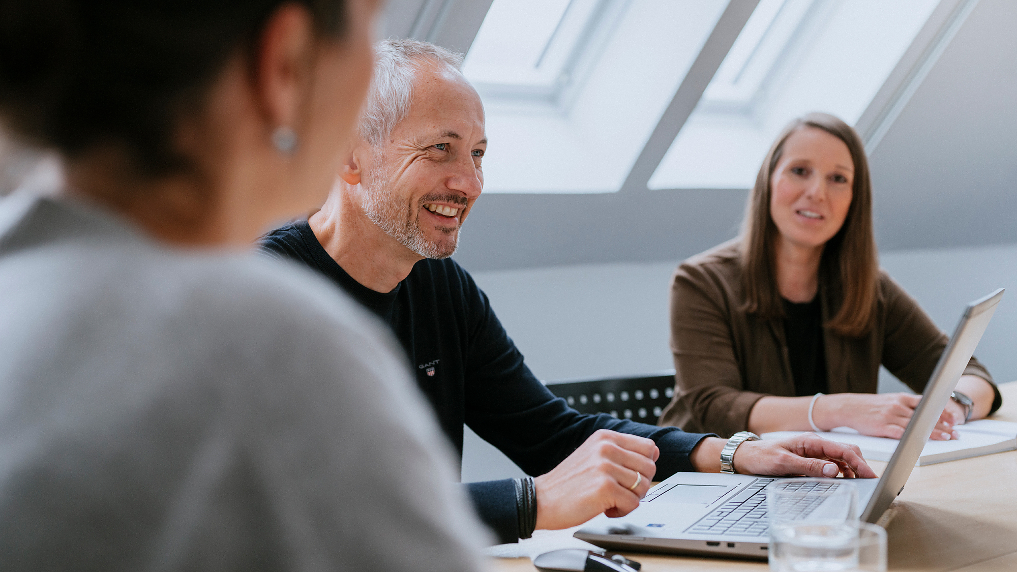 Ein Mann und zwei Frauen sitzen an einem Besprechungstisch